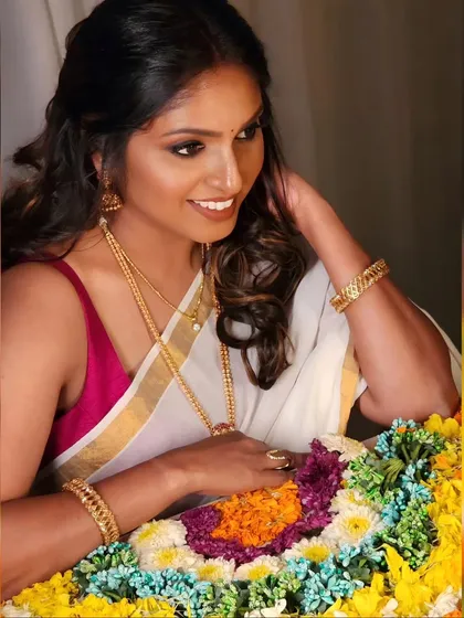 A happy Onam celebration. The simple white and gold saree is paired with a pop of color from the blouse and beautiful gold jewellery.