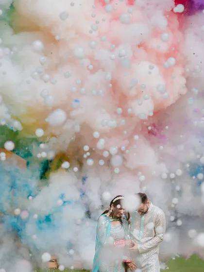 A creative shot capturing a couple surrounded by a cloud of colorful smoke bombs, adding a modern and dramatic twist to their Haldi portraits.