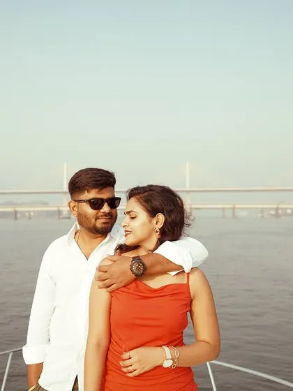 A candid shot of a couple enjoying the view from the bow of a yacht. The bridge in the background adds a sense of place to this destination photoshoot in Goa.
