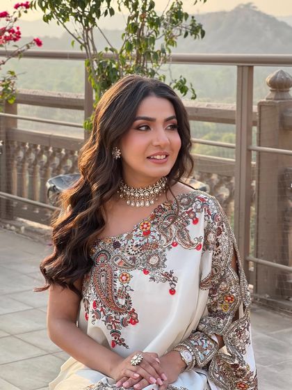A bride at her Mehandi, her hair in soft, flowing waves that complement her elegant one-shoulder saree.