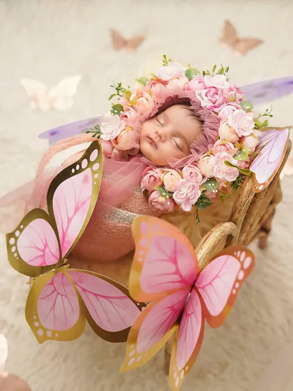 The baby butterfly is ready to fly! This whimsical setup includes a floral bonnet, a cozy wrap, and beautiful paper butterflies.
