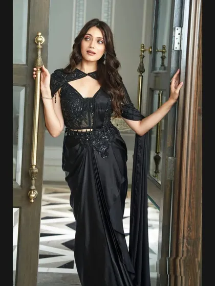 Posed in a doorway, this image highlights the chic silhouette of the black pre-draped saree, perfect for making a grand entrance.
