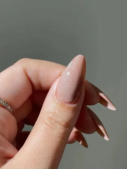 A close-up detail of the shimmering nude polish on a long stiletto nail, showing the fine, reflective glitter within the gel.