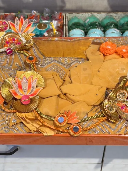 An elegant yellow suit, perfect for a pre-wedding function, is packed on a decorative tray. The lotus-themed gota work embellishments add a touch of auspiciousness and beauty to the gift.