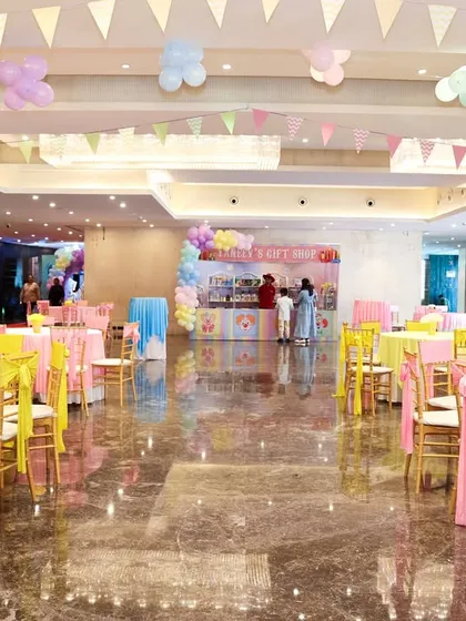 A wide view of the party hall, showing the colorful table settings and festive bunting hanging from the ceiling.