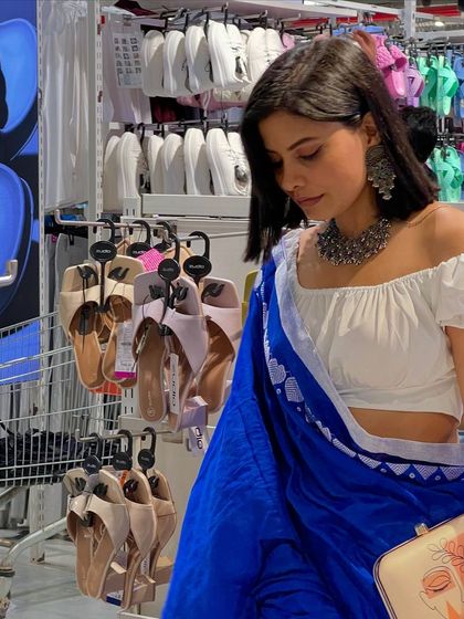 Another angle of this stylish shopping trip. The neutral tone of the clutch makes it a versatile accessory that pairs well with both the vibrant saree and the modern, off-shoulder blouse.