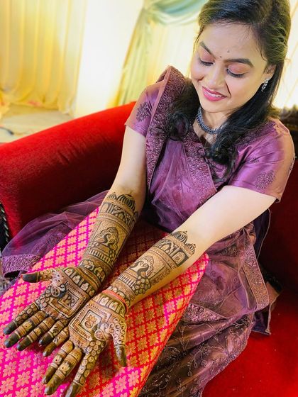 A smiling bride proudly displaying her full-arm traditional mehndi. The design is intricate and perfectly suited for her special day.