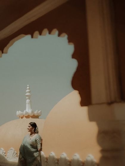 A solo portrait of the bride looking out from a heritage balcony. The architectural framing and soft light create a pensive and elegant image.