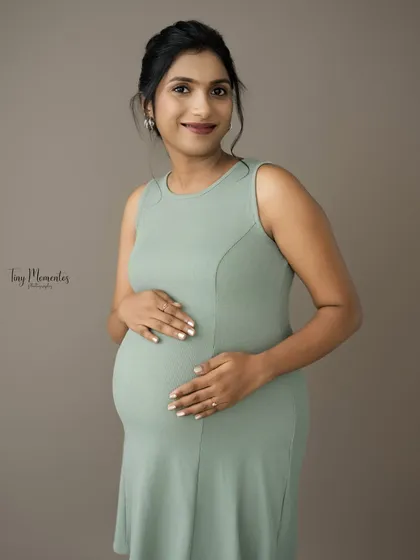 A simple, heartfelt portrait. The focus is on the mother's warm smile and the gentle way she holds her baby bump.
