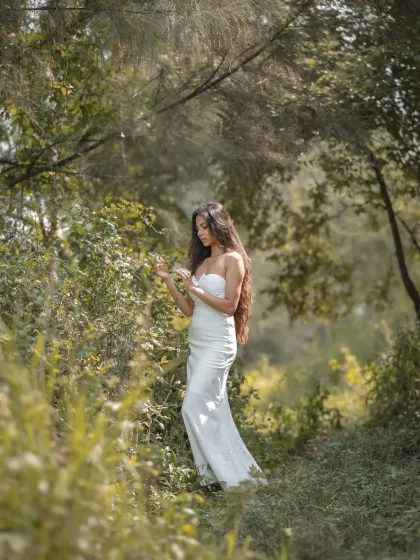 A dreamy, editorial bridal shoot in a lush, green forest. The soft focus and natural environment give this photo a fairytale-like quality.