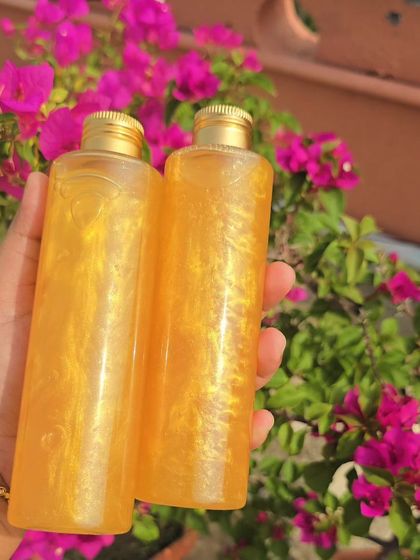 My shimmering Gold Facewash, held against a backdrop of beautiful flowers. This gentle cleanser not only removes impurities but also leaves a subtle, radiant glow on your skin after every wash.
