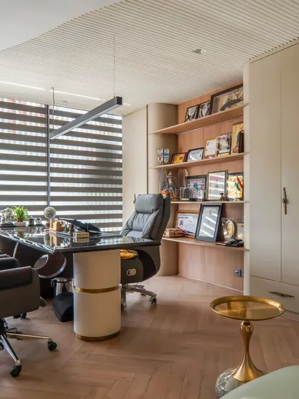 The director's cabin in the office, designed with a sophisticated palette and herringbone wooden flooring. The custom shelving is designed to display awards and personal items, making the space feel curated.