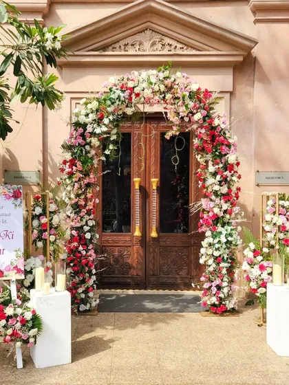 A classic floral arch frames the main entrance, using a mix of red, pink, and white roses to create a romantic and timeless welcome.