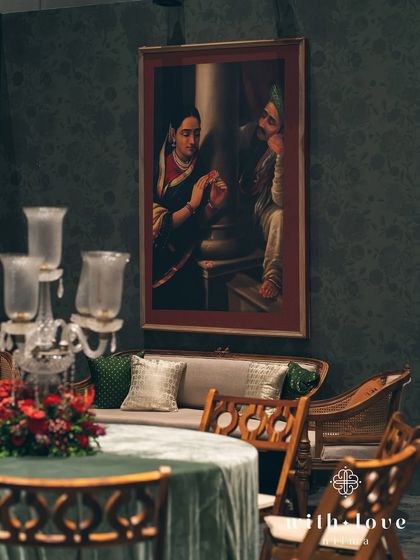 A detail of the seating, with a candelabra centerpiece and a Raja Ravi Varma painting in the background. The composition highlights the layers of art and decor.