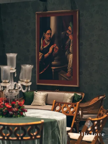 A detail of the seating, with a candelabra centerpiece and a Raja Ravi Varma painting in the background. The composition highlights the layers of art and decor.