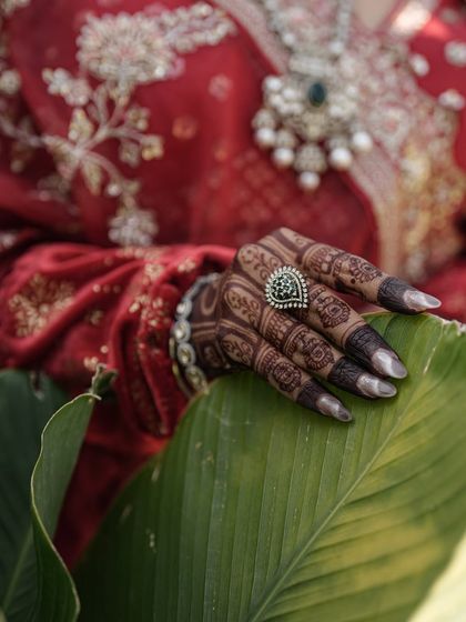 An artistic shot of the bride's hand, showing the gorgeous contrast between the dark henna stain, her red lehenga, and the green leaf.