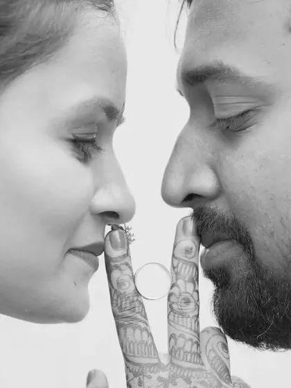 A creative and intimate black-and-white photo of a couple, their faces close as they playfully interact with their engagement rings.