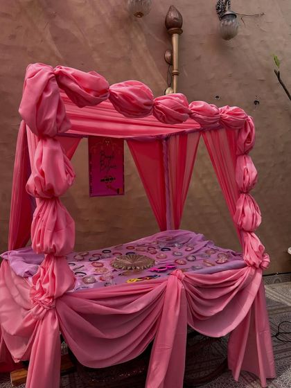 A cozy and decorative seating arrangement for a home Haldi, featuring a bed draped in shades of pink fabric.