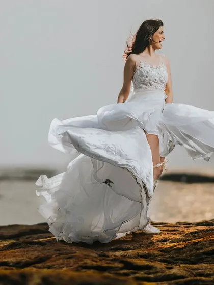A bridal portrait full of movement and life. The bride's dress is caught by the sea breeze, creating a dynamic and free-spirited image against the ocean backdrop.