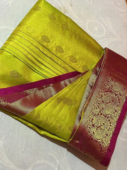 A vibrant lime green silk saree with a pink and gold border, folded to highlight its beautiful colors.
