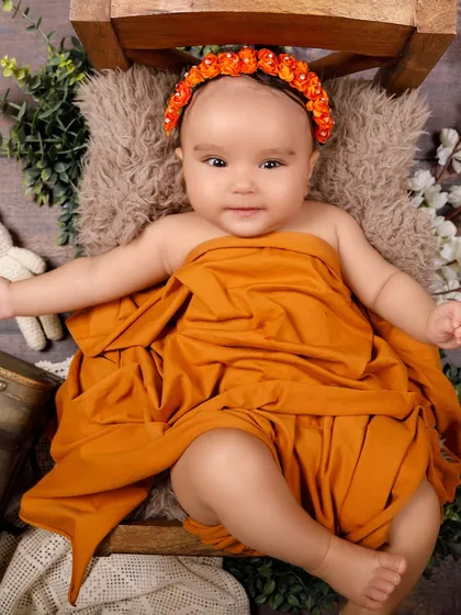This awake baby girl, wrapped in an orange cloth, is ready for her close-up. Her bright eyes and happy expression are captivating.