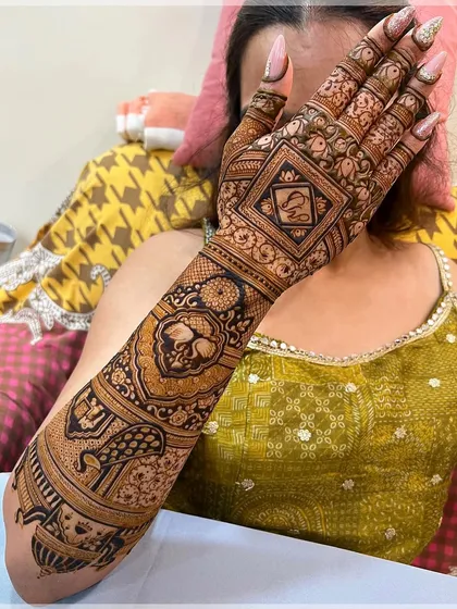 This design features the initial 'S' in a diamond-shaped frame, with the rest of the arm adorned with floral and peacock motifs.