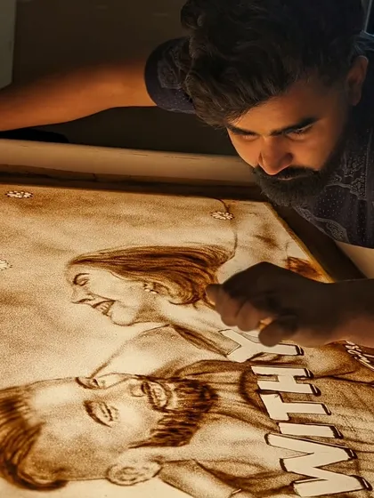 Deep in the process of creating the 'With You' sand art, focusing on the expressions.