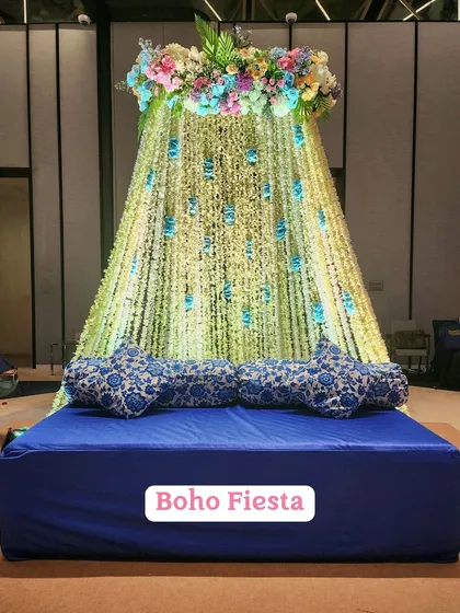 This "Boho Fiesta" Mehendi setup features a canopy of hanging floral strings over a comfortable floor seating arrangement with traditional printed cushions.