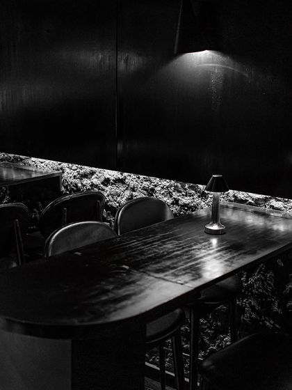 Dine in the mystique of a minimalist, modern-day den. The combination of raw, cave-like walls and sleek, dark furniture creates a uniquely sophisticated dining environment.