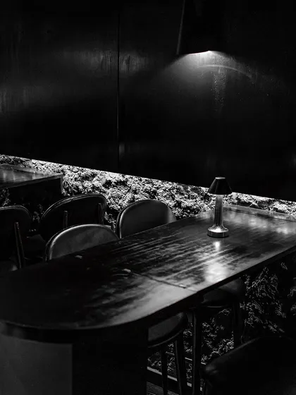 Dine in the mystique of a minimalist, modern-day den. The combination of raw, cave-like walls and sleek, dark furniture creates a uniquely sophisticated dining environment.