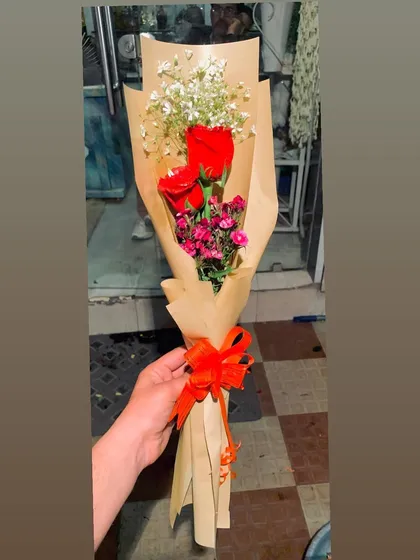 A rustic hand-tied bouquet with two red roses and other small filler flowers. The simple brown paper wrapping makes it a charming and understated gesture.