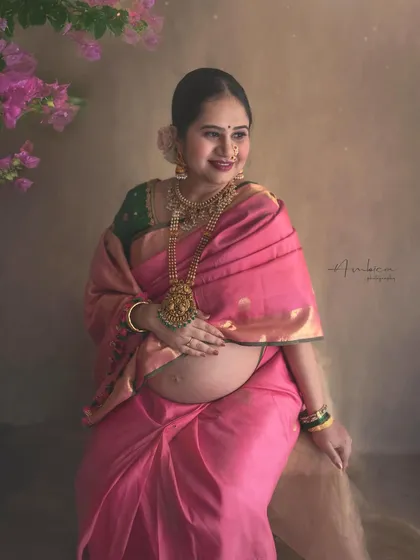 Radiating joy and serenity, this close-up portrait in a pink Kanchipuram saree highlights the beautiful glow of pregnancy. The traditional temple jewelry and floral hairpiece complete this classic, ethnic maternity look.