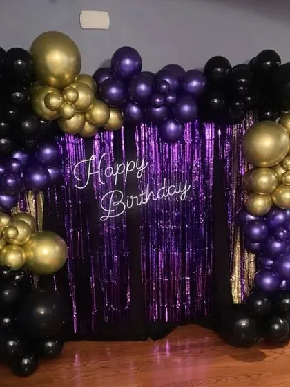 A bold and dramatic birthday backdrop. This setup features a purple tinsel curtain with a "Happy Birthday" sign, framed by a black, purple, and gold balloon arrangement for a touch of dark glamour.