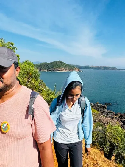 A close-up of two trekkers on the trail, with the blue sea and coastline in the background.