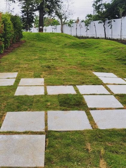 A playful pattern of square stone pavers is scattered across a rolling green lawn. This design breaks up the monotony of the grass and creates an informal, interactive pathway that invites exploration.