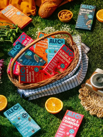 A beautiful picnic flatlay for Alt Co. chocolates. The wicker basket, fresh oranges, and sunny lighting create a wholesome and joyful scene, perfect for brand storytelling.