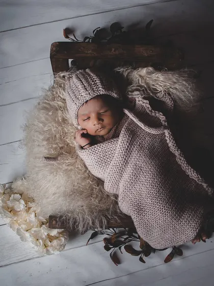A rustic-themed shot with a baby in a knitted bonnet sleeping in a wooden crate. The moody lighting and simple props create a timeless, natural feel.