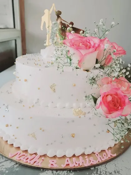 We love the festive vibes of wedding season. This two-tier engagement cake is adorned with fresh pink roses and a romantic couple topper, creating a beautiful centerpiece for the happy couple.