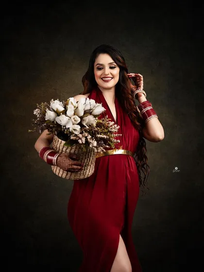 A beautiful portrait of a mom-to-be in a red gown, holding a basket of white roses. The traditional bangles (chooda) add a lovely personal and cultural touch to the image.