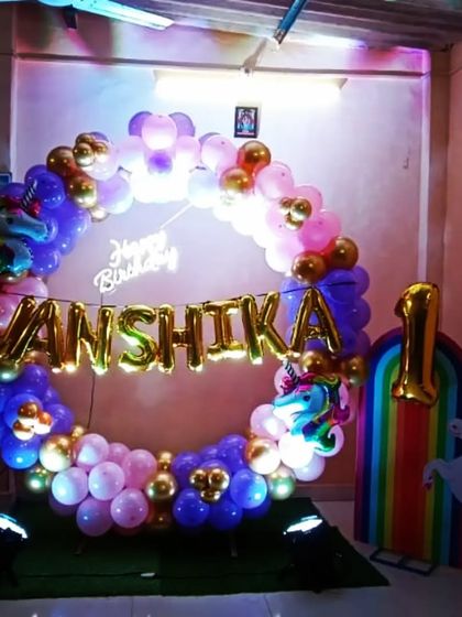 A unicorn-themed first birthday party with a magical ring decoration. The setup includes a rainbow-colored balloon arch, unicorn props, and a 'Happy Birthday' neon sign.