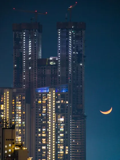 A zoomed-in shot of the crescent moon next to the top of the Palais Royale skyscraper at night.