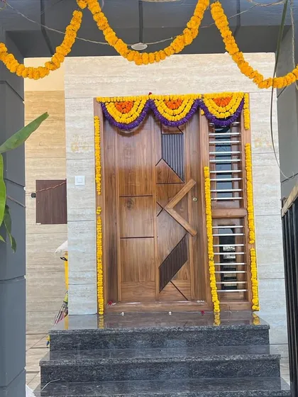 The main entrance of the Kantraj residence, decorated for the housewarming ceremony. The custom-designed teakwood door with its geometric patterns serves as a beautiful focal point for the home's facade.