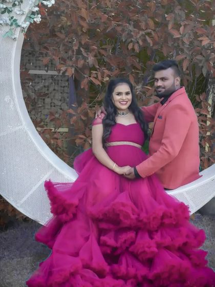 A glamorous couple's portrait on the crescent moon prop. The mom-to-be's vibrant magenta gown looks stunning against the white moon and natural background.