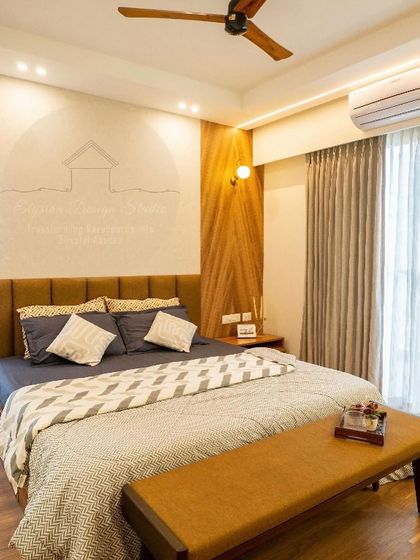 A master bedroom that exudes quiet luxury. The design features a custom upholstered headboard, a chevron-patterned wood panel beside the bed, and a comfortable bench at the foot of the bed.