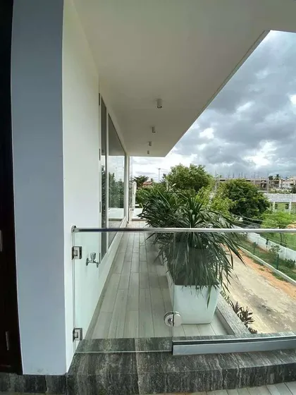 This long balcony in Mysore uses large, modern white planters to create a clean and minimalist look. The plants are chosen to withstand the elements and provide a consistent green border along the glass railing.