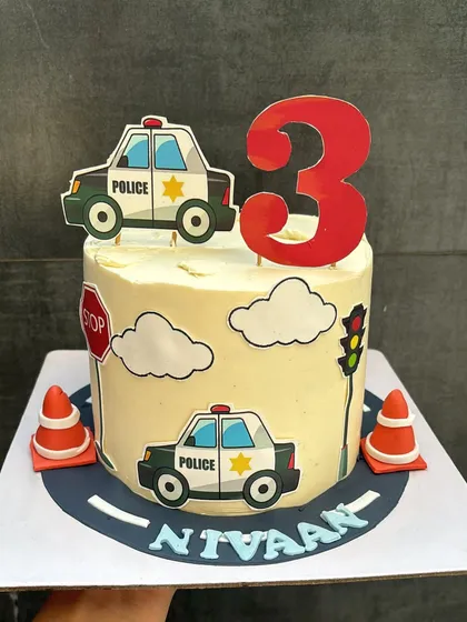 A fun police car themed cake for a 3rd birthday. This 1.5 kg Chocolate & Biscoff cake is decorated with edible traffic signs, clouds, and police cars for a delightful celebration.