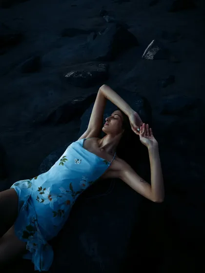 A serene, almost painterly shot from a sunset beach editorial. The deep blue tones of twilight and the model's relaxed pose create a peaceful and beautiful image.