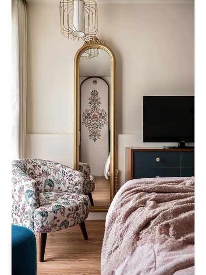 A cozy corner of the master bedroom, featuring a comfortable floral armchair and a traditional gold-framed mirror. This space is perfect for reading or relaxing.