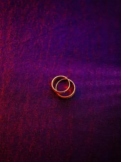 An artistic photo of two wedding bands intertwined on a textured, colorful surface. The lighting creates a moody and romantic feel.
