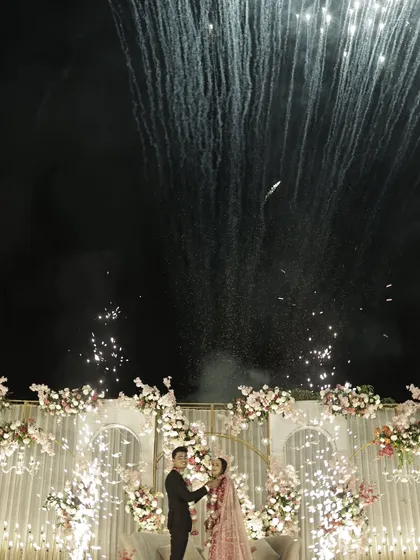 A wide-angle view of the couple's reception stage, lit up by a stunning fireworks display.